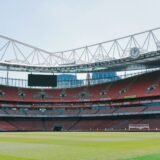 Teren de fotbal văzut din tribună în timpul unui meci, cu jucătorii așezați în formație