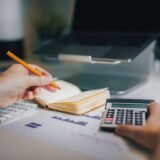 Doi parteneri de afaceri își strâng mâna deasupra unui birou cu documente, după o negociere reușită