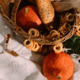 Pătură de picnic întinsă pe iarbă într-un parc, cu un coș de răchită, fructe și sandvișuri