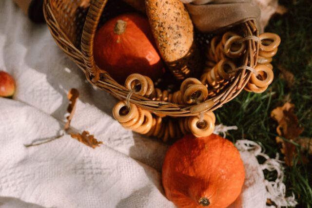 Pătură de picnic întinsă pe iarbă într-un parc, cu un coș de răchită, fructe și sandvișuri