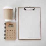 Calculator, carnet cu notițe și o cană de cafea pe un birou, pregătite pentru calculul prețului unui serviciu