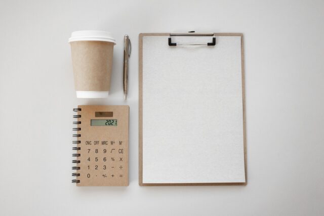 Calculator, carnet cu notițe și o cană de cafea pe un birou, pregătite pentru calculul prețului unui serviciu